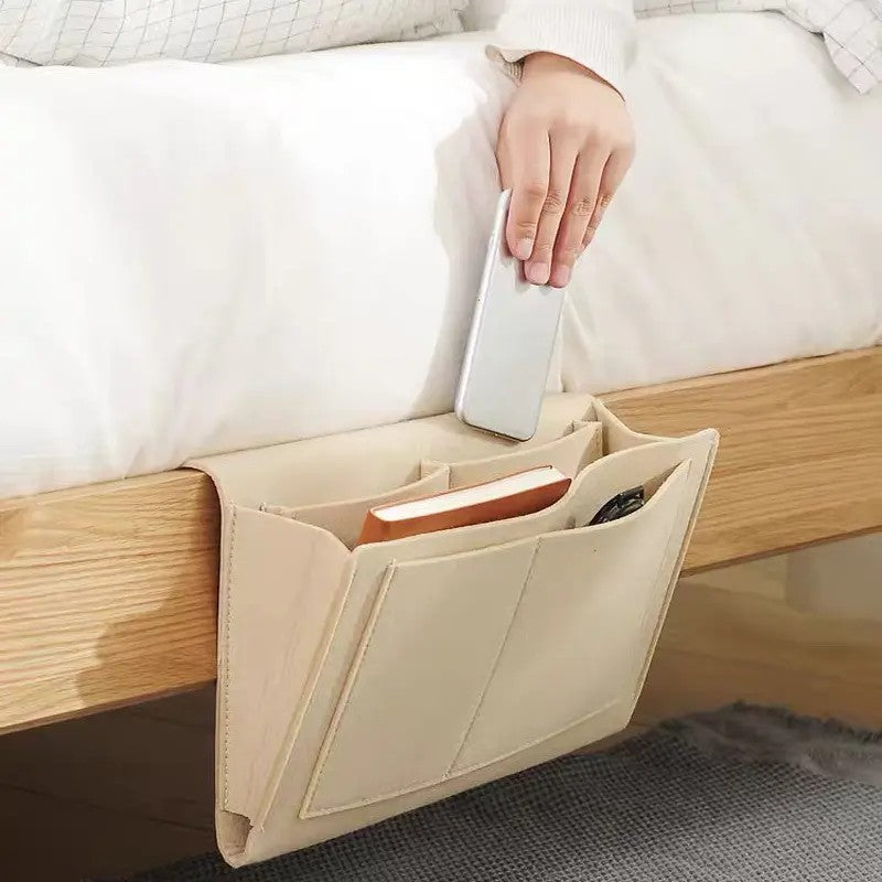 Beige five-pocket bedside organizer holding a phone, book and remote beside a bed
