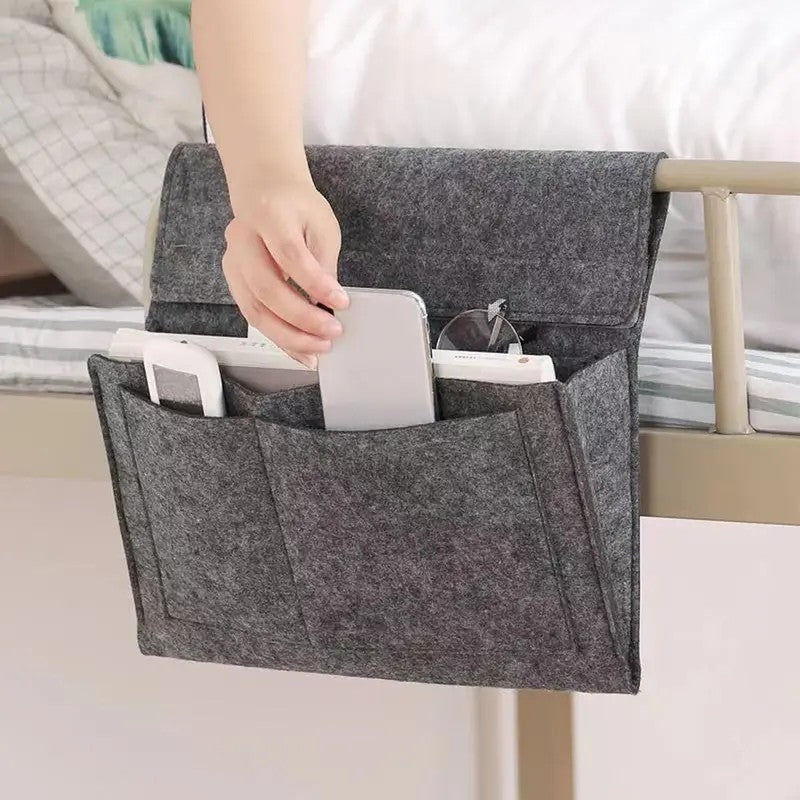 Grey felt bedside organizer attached to a metal bunk-bed rail and holding electronics and glasses